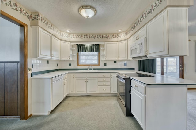 kitchen with kitchen peninsula, white cabinetry, sink, and white appliances