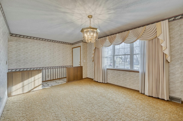 carpeted empty room with a textured ceiling and an inviting chandelier