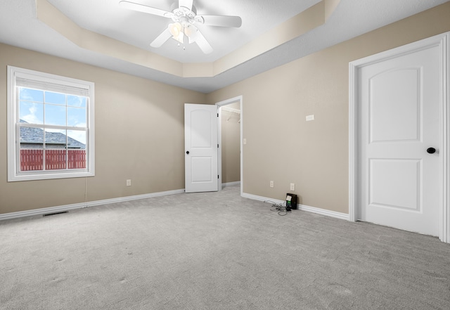 spare room with a raised ceiling, ceiling fan, and light carpet