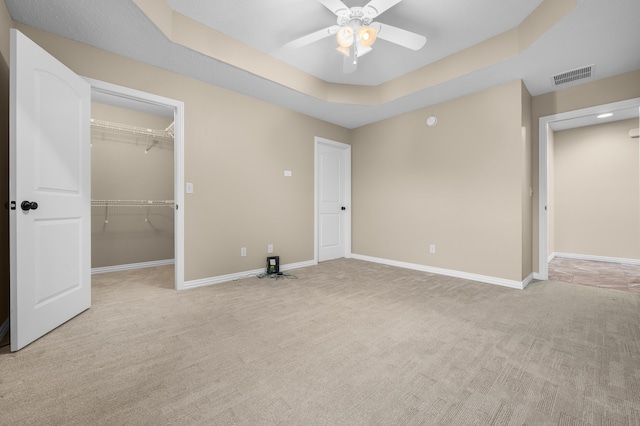 unfurnished bedroom with light carpet, a closet, a tray ceiling, and ceiling fan