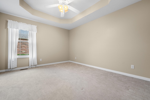 spare room with a tray ceiling, a wealth of natural light, carpet, and ceiling fan