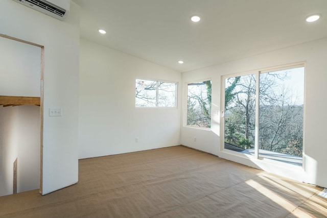 empty room featuring a wall unit AC, light colored carpet, a healthy amount of sunlight, and lofted ceiling