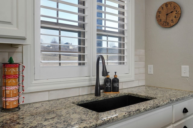 details with backsplash, light stone countertops, sink, and white cabinetry