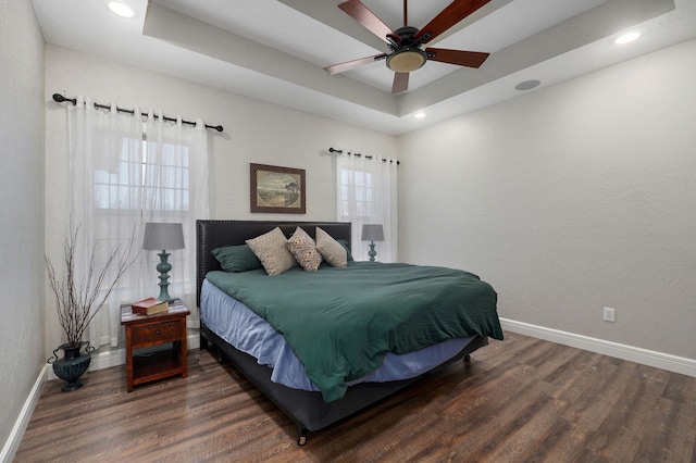 bedroom featuring ceiling fan, multiple windows, dark wood-type flooring, and a tray ceiling