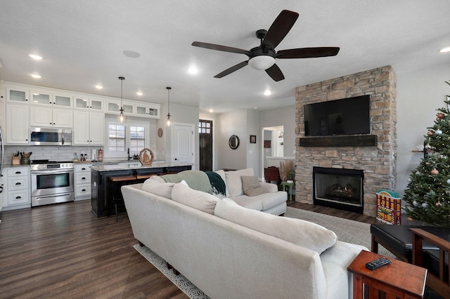 living room featuring dark hardwood / wood-style floors, a stone fireplace, ceiling fan, and sink