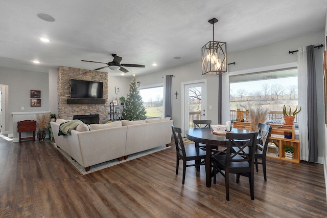 dining area with a textured ceiling, ceiling fan with notable chandelier, a fireplace, and dark wood-type flooring