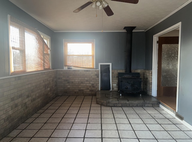 unfurnished living room featuring light tile patterned flooring, ornamental molding, brick wall, and a wood stove