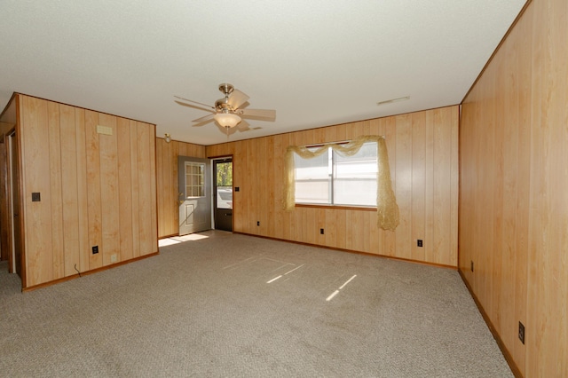 interior space with wood walls, ceiling fan, and light colored carpet