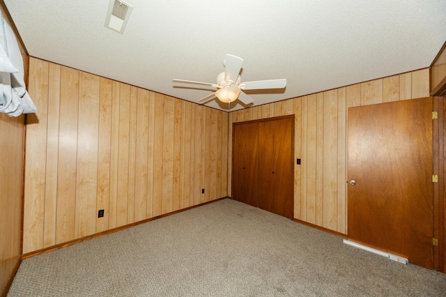 unfurnished bedroom with light colored carpet, ceiling fan, and wooden walls