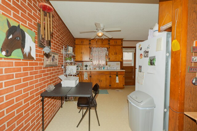 kitchen featuring sink, white fridge, ceiling fan, and brick wall