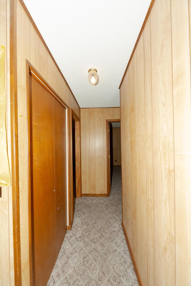 hallway featuring wooden walls, crown molding, and light carpet