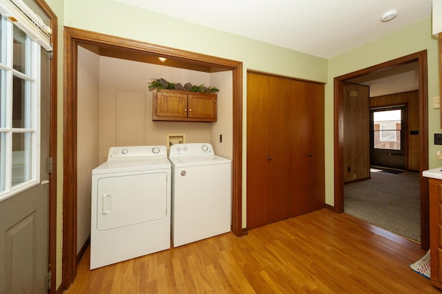 clothes washing area with separate washer and dryer, light hardwood / wood-style flooring, and cabinets