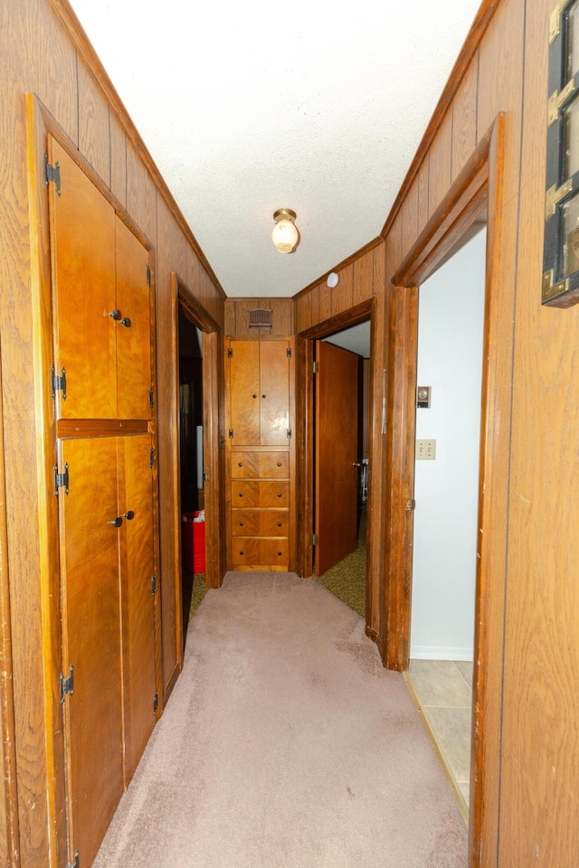 hallway with wood walls, light colored carpet, and ornamental molding