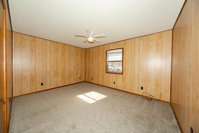 unfurnished room featuring ceiling fan, wooden walls, and light colored carpet