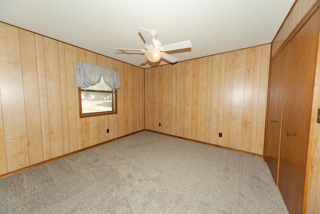 carpeted spare room featuring ceiling fan and wood walls