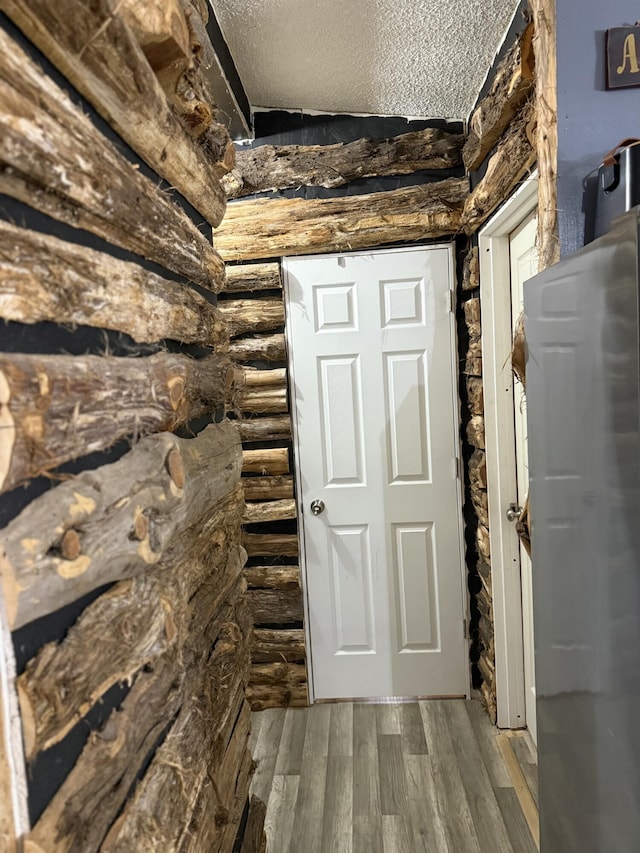 corridor featuring rustic walls, a textured ceiling, and hardwood / wood-style flooring