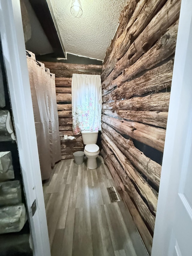 bathroom featuring a textured ceiling, toilet, wood-type flooring, and rustic walls