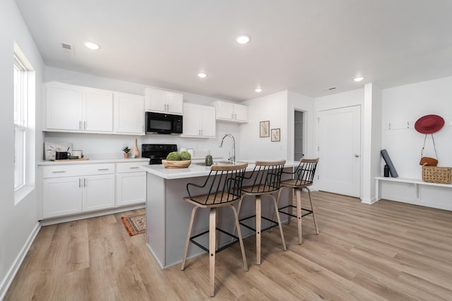 kitchen with black appliances, light hardwood / wood-style flooring, white cabinets, a breakfast bar area, and an island with sink