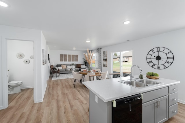 kitchen featuring gray cabinetry, dishwasher, sink, a kitchen island with sink, and light wood-type flooring