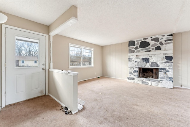 foyer entrance with a stone fireplace, a wealth of natural light, carpet floors, and a textured ceiling