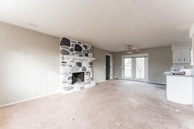 unfurnished living room featuring a stone fireplace, wooden walls, carpet flooring, ceiling fan, and a textured ceiling