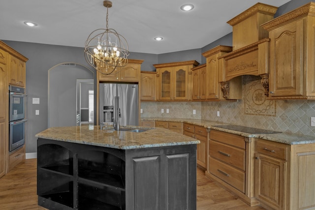 kitchen featuring light stone countertops, appliances with stainless steel finishes, a center island with sink, and light hardwood / wood-style flooring