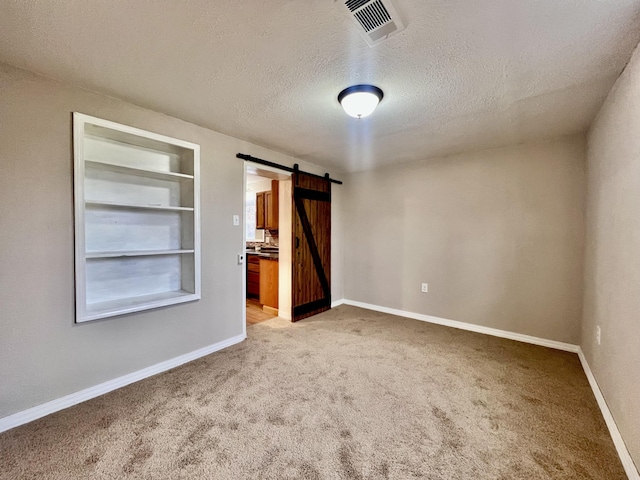 unfurnished bedroom featuring a barn door, light colored carpet, and a textured ceiling