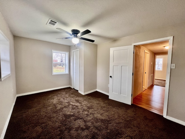 unfurnished bedroom with ceiling fan, a textured ceiling, and dark colored carpet