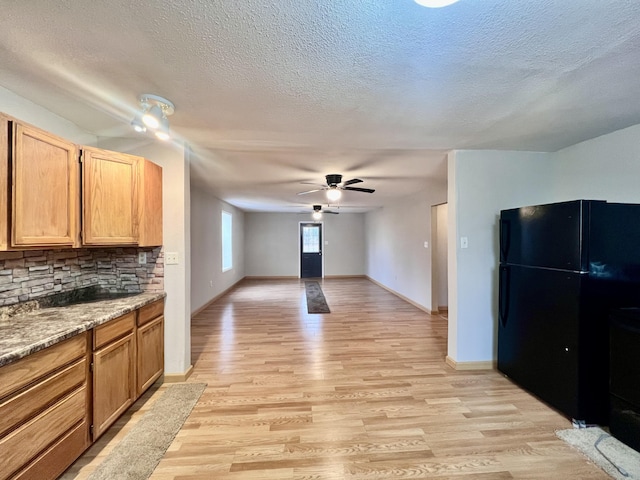 kitchen with light stone countertops, ceiling fan, tasteful backsplash, black fridge, and light hardwood / wood-style floors