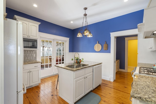 kitchen with white appliances, a kitchen island with sink, sink, decorative light fixtures, and white cabinetry