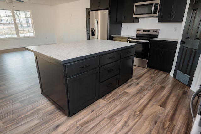 kitchen featuring hardwood / wood-style floors, ceiling fan, a kitchen island, and appliances with stainless steel finishes