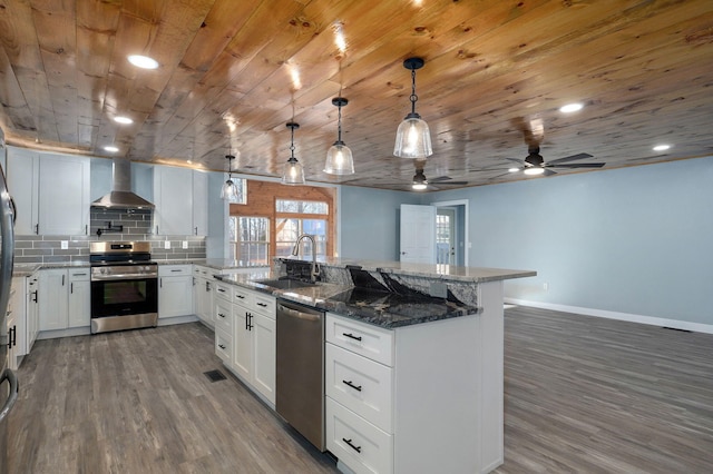 kitchen featuring appliances with stainless steel finishes, wall chimney range hood, sink, decorative light fixtures, and white cabinets