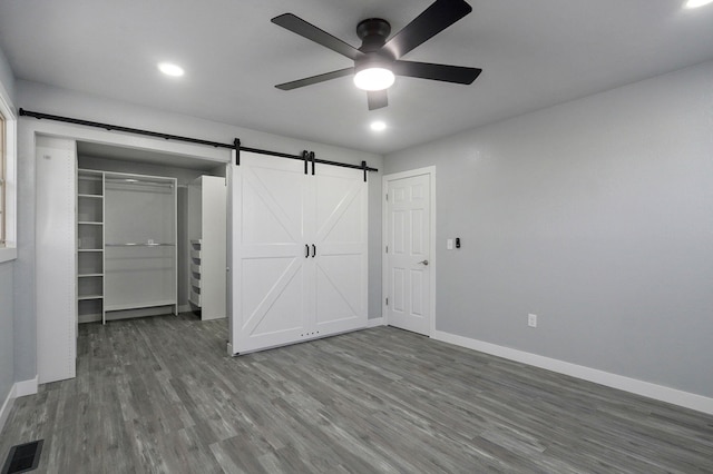 empty room with a barn door, hardwood / wood-style floors, and ceiling fan