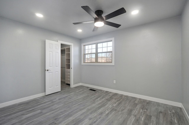 unfurnished bedroom with a walk in closet, wood-type flooring, a closet, and ceiling fan