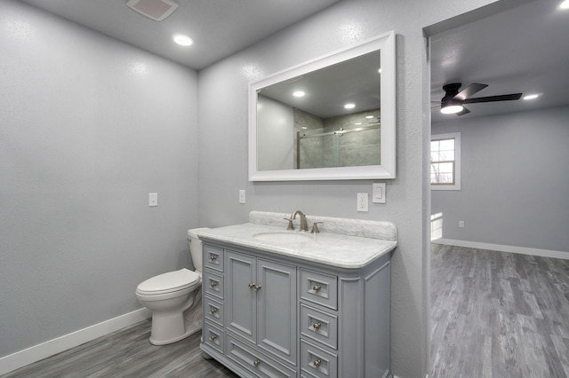 bathroom with wood-type flooring, vanity, ceiling fan, walk in shower, and toilet