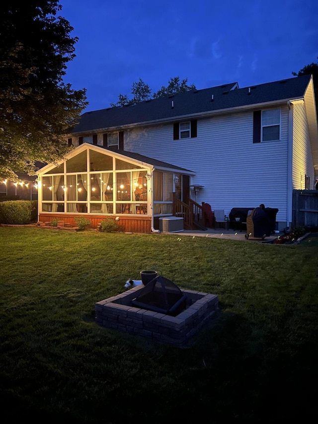 back house at dusk featuring a sunroom and a lawn