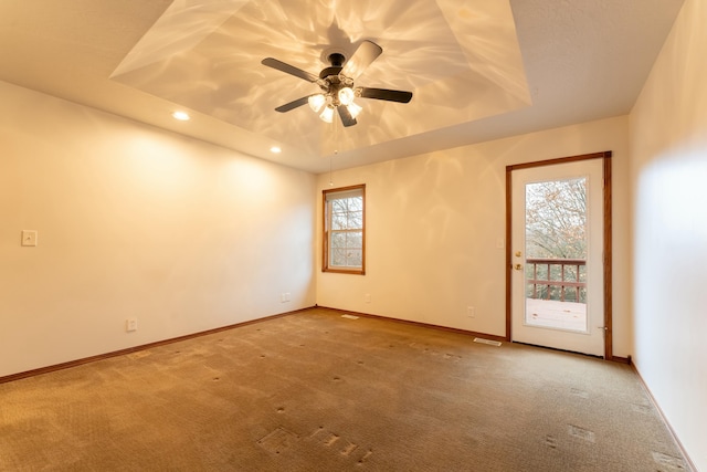 carpeted spare room featuring ceiling fan, a wealth of natural light, and a tray ceiling