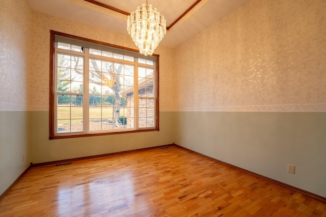 empty room featuring lofted ceiling, light wood-type flooring, and a chandelier