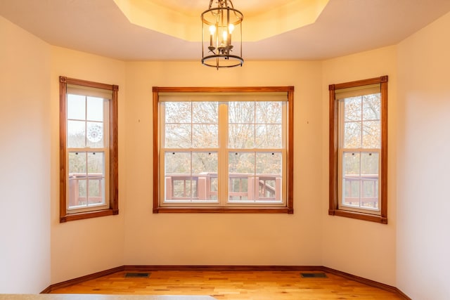 spare room featuring a notable chandelier, a raised ceiling, and light hardwood / wood-style flooring