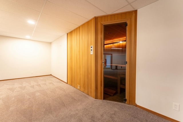 interior space with wood walls, a drop ceiling, and carpet floors