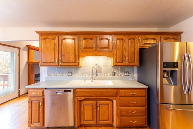 kitchen with tasteful backsplash, sink, light hardwood / wood-style floors, and appliances with stainless steel finishes