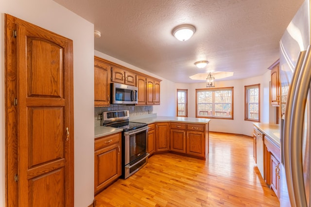 kitchen featuring kitchen peninsula, decorative backsplash, a textured ceiling, stainless steel appliances, and light hardwood / wood-style floors