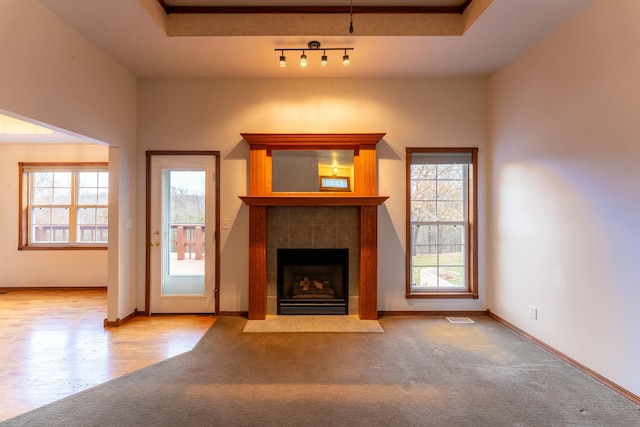 unfurnished living room with light carpet, a raised ceiling, and a tiled fireplace