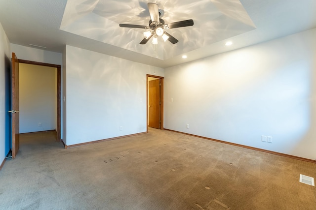 carpeted spare room with a tray ceiling and ceiling fan