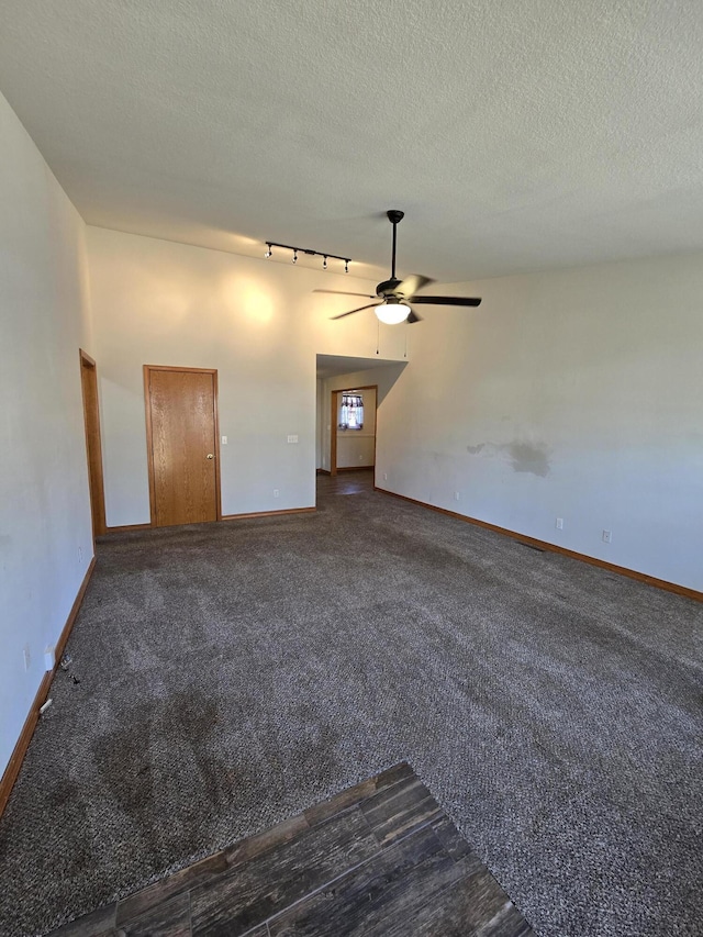 unfurnished room featuring a textured ceiling, ceiling fan, track lighting, and dark colored carpet