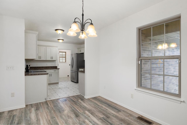 kitchen with stainless steel refrigerator, light hardwood / wood-style flooring, a chandelier, pendant lighting, and white cabinets