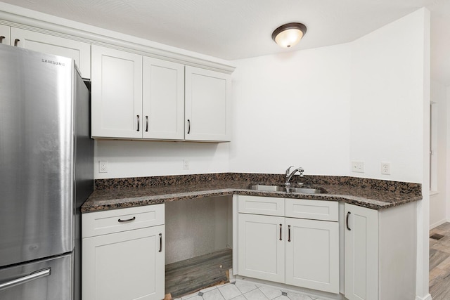 kitchen with stainless steel refrigerator, sink, light hardwood / wood-style flooring, dark stone countertops, and white cabinets