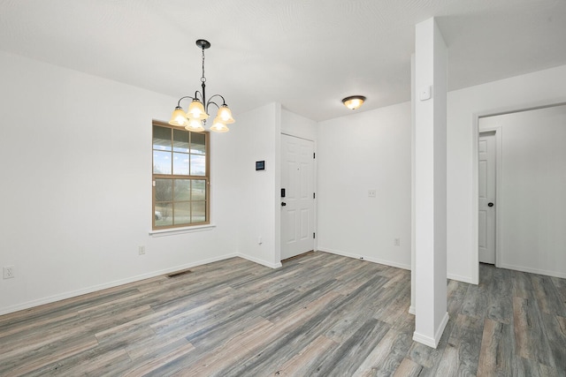 spare room with dark hardwood / wood-style floors and an inviting chandelier