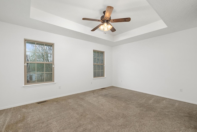 carpeted spare room featuring a tray ceiling and ceiling fan