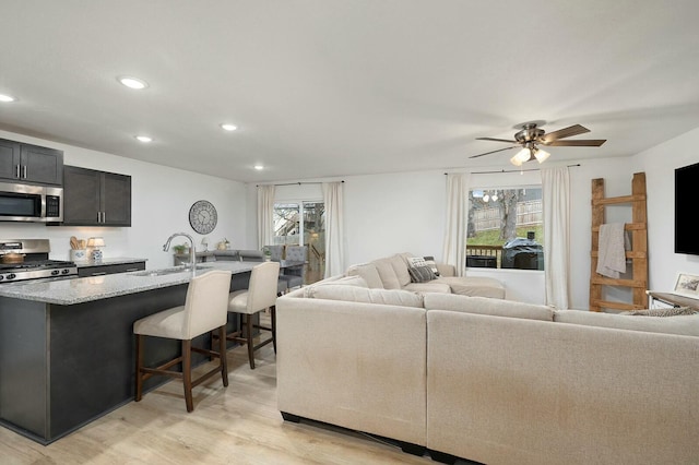 living room with ceiling fan, sink, and light wood-type flooring